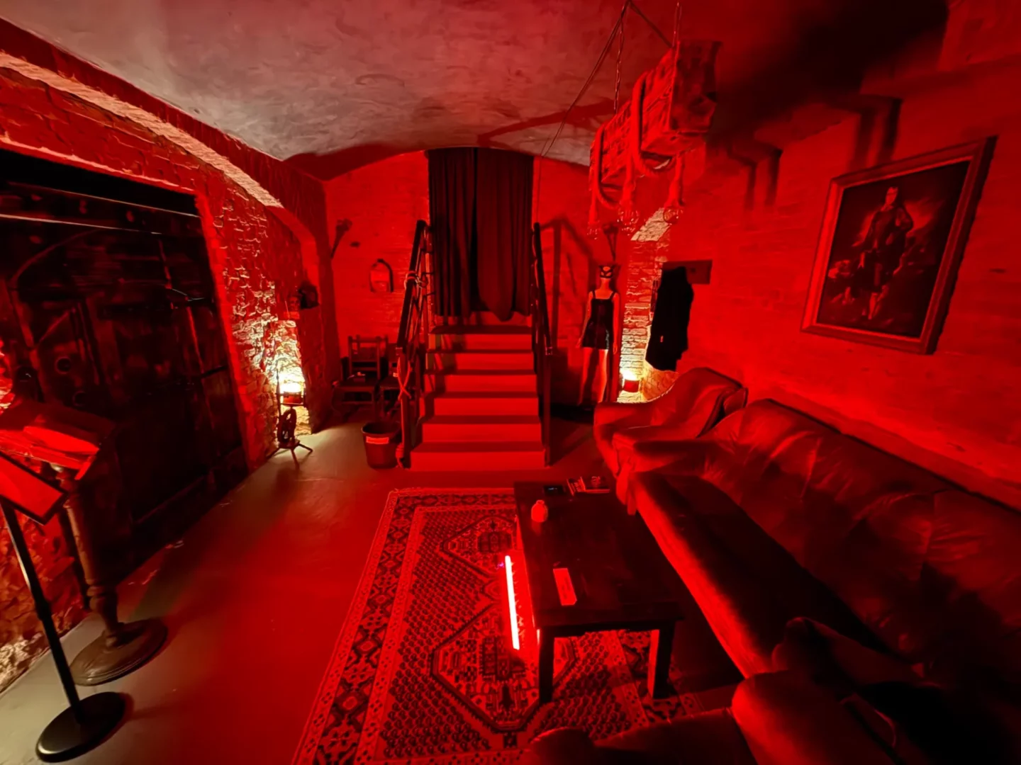 A basement lounge with a staircase, a sofa, and a mannequin wearing a mask; BDSM studio in Vinohrady, Prague 2