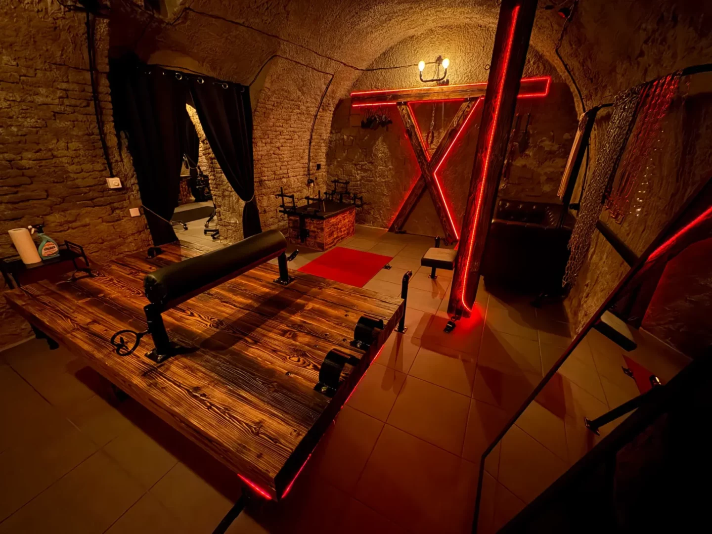 Spielzimmer mit einem hölzernen Andreaskreuz, einer Bondage-Bank und einer roten Neonleuchte, BDSM-Studio Karlín, Prag 8