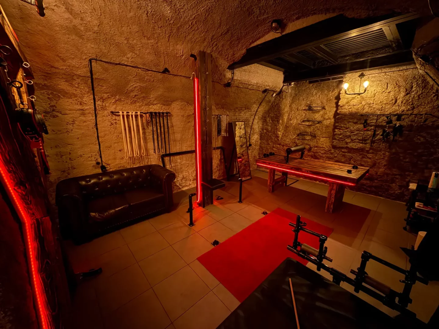Spielzimmer mit Ledersofa, einer Wand mit Seilen für Shibari und einer Bondage-Bank, BDSM-Studio Karlín, Prag 8
