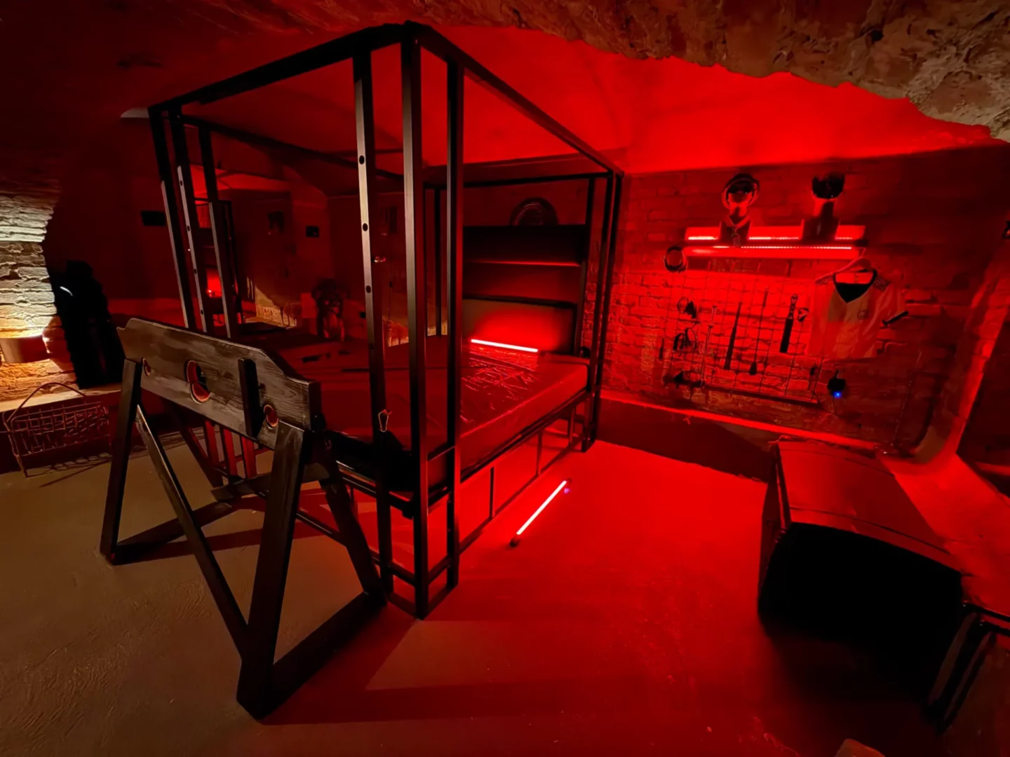Sklepní dungeon s kovovou bondage postelí a dřevěnou kládou, BDSM studio Vinohrady, Praha 2
