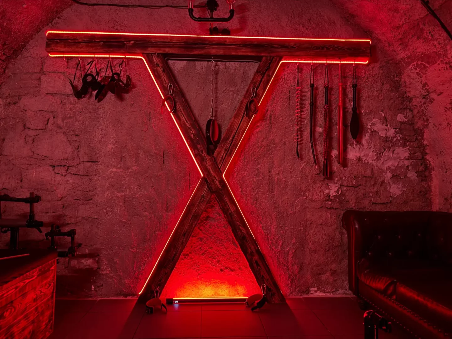 Ein hölzernes Andreaskreuz mit Neonbeleuchtung und Peitschen an der Wand, BDSM-Studio Karlín, Prag 8