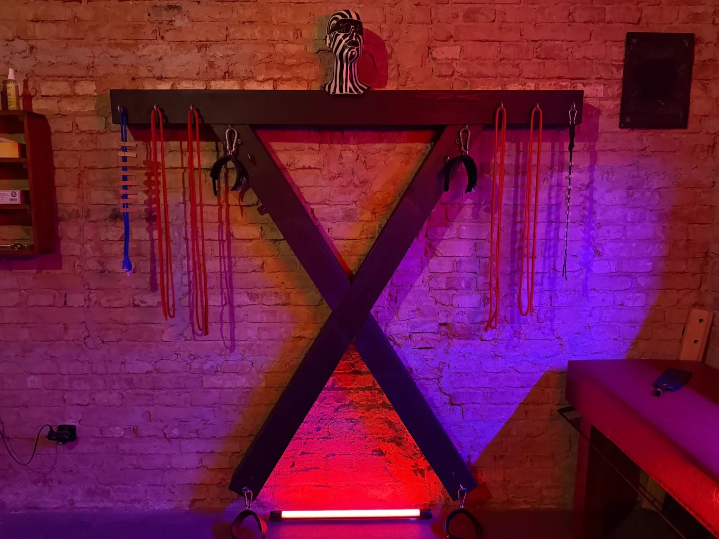Dřevěný ondřejský kříž s pouty a lany na cihlové zdi, BDSM studio Vinohrady, Praha 2
