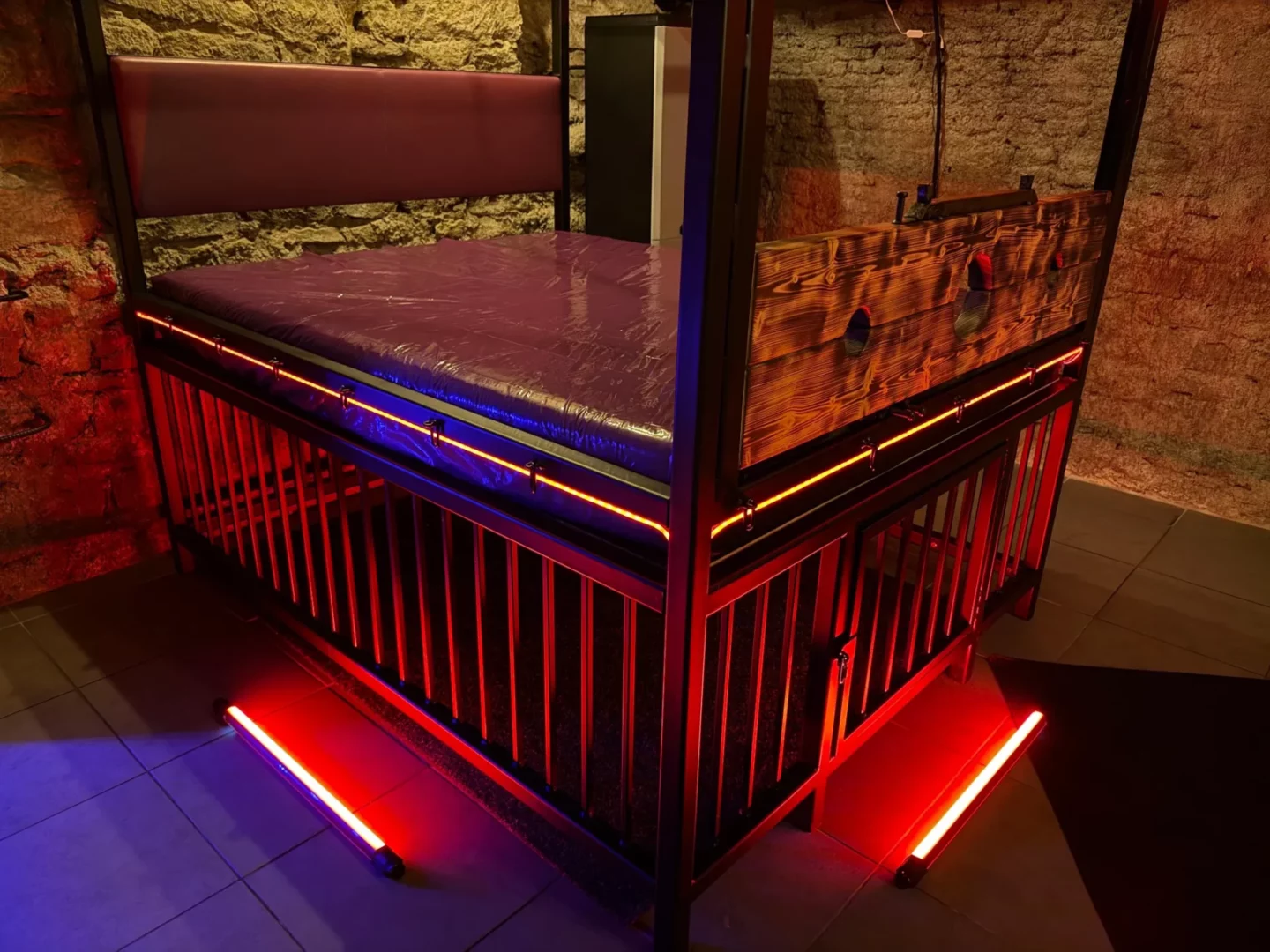 Detailansicht eines Bettes mit schwarzer Matratze, einem Holzklotz und einem Käfig, BDSM-Studio Karlín, Prag 8